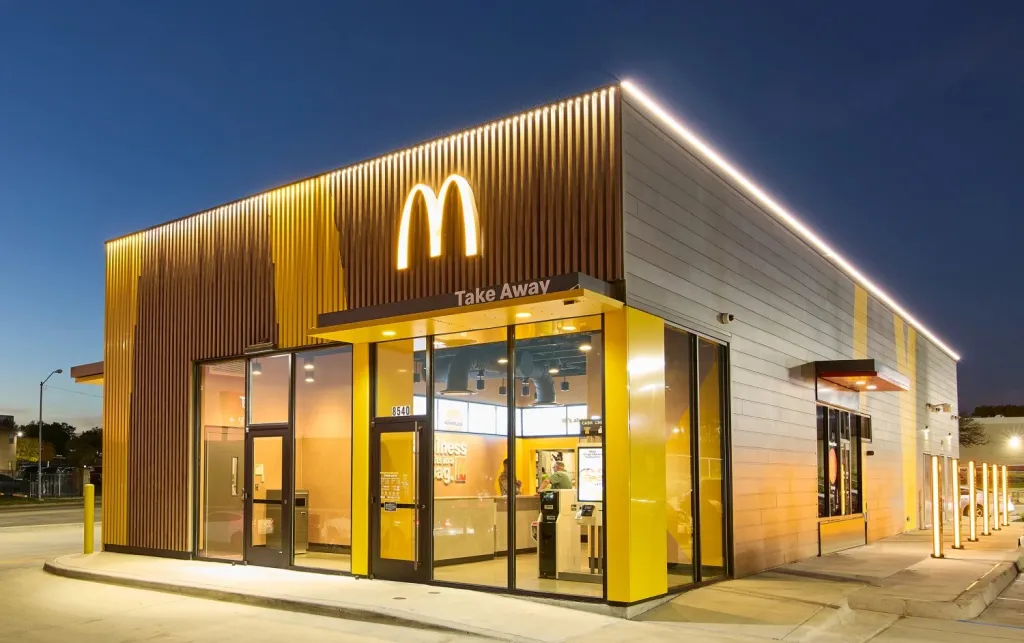 New McDonald's facade with a yellow and brown slatted exterior, illuminated McDonald's arches logo, and 
