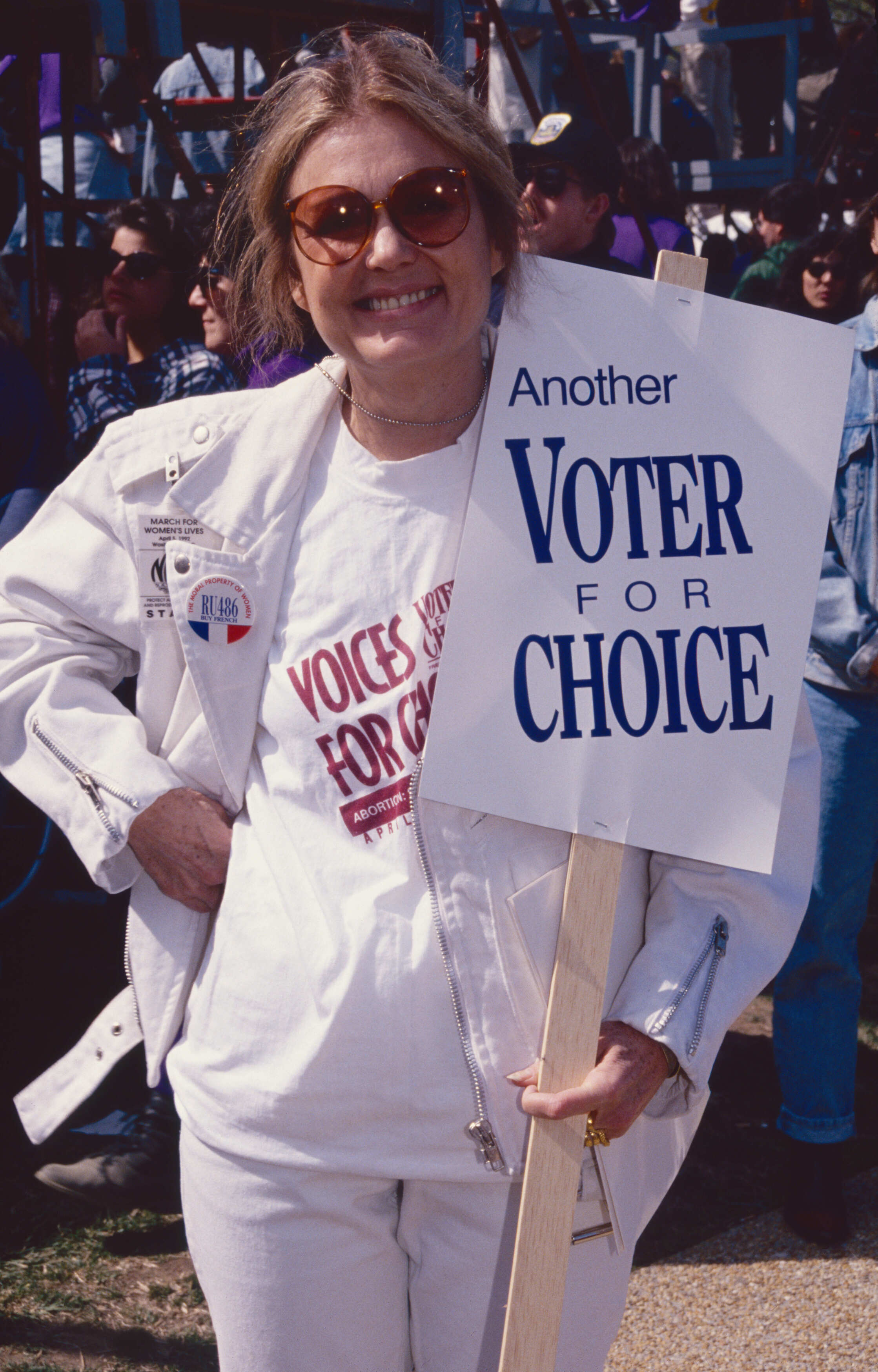 Gloria Steinem smiling and holding a sign that reads 