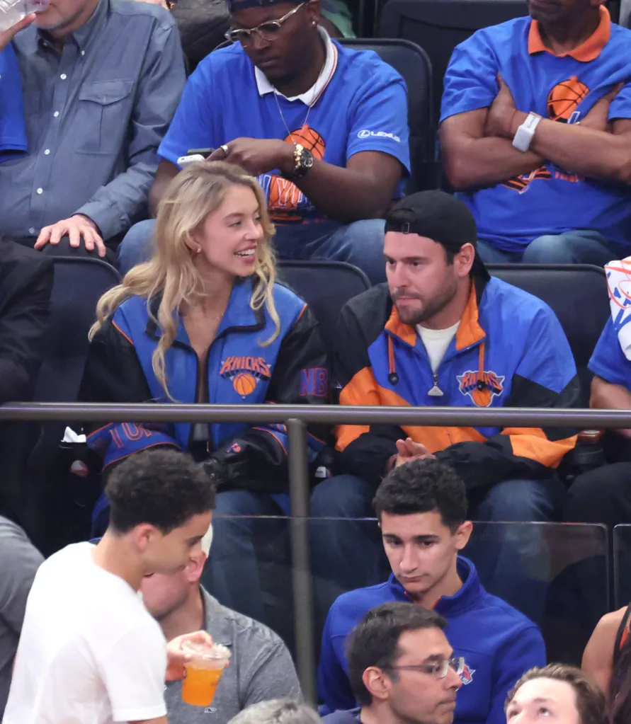 Sydney Sweeney, in a blue Knicks jacket, and Scooter Braun, in ablack cap and a blue and orange Knicks jacket, at an NBA Finals game.