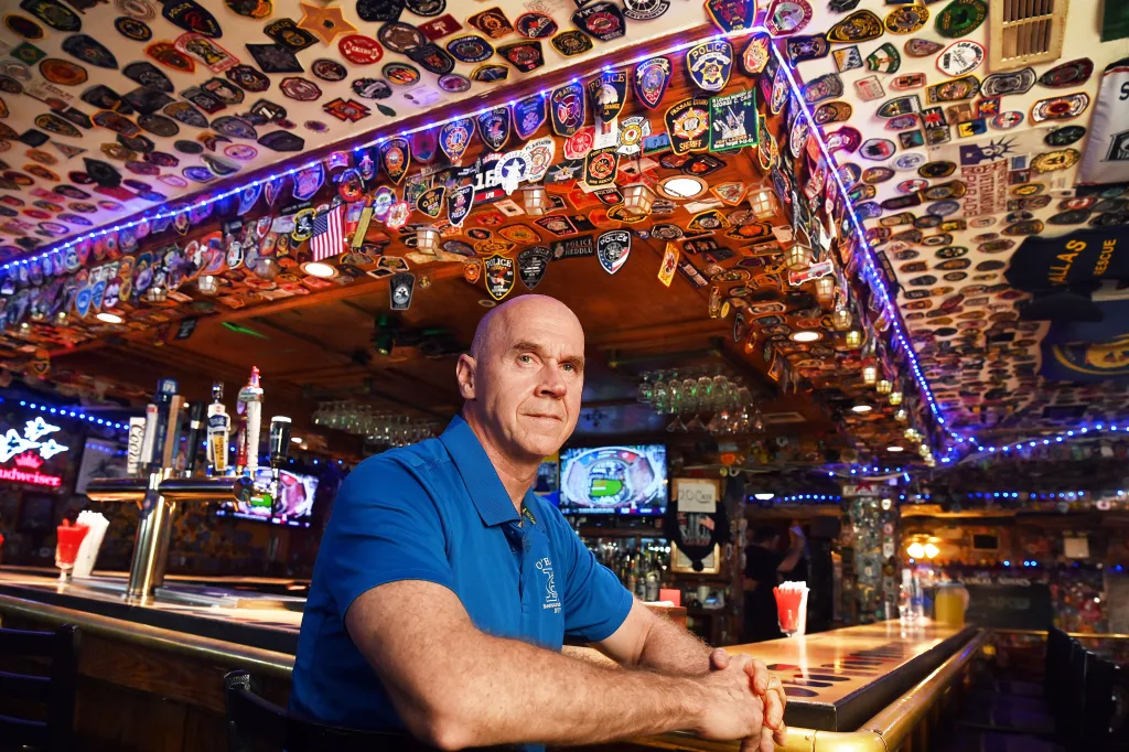 Michael Keane, co-owner of O'Hara's Bar & Restaurant, sits at the bar with ceilings and walls covered in over 7,000 first responder patches.