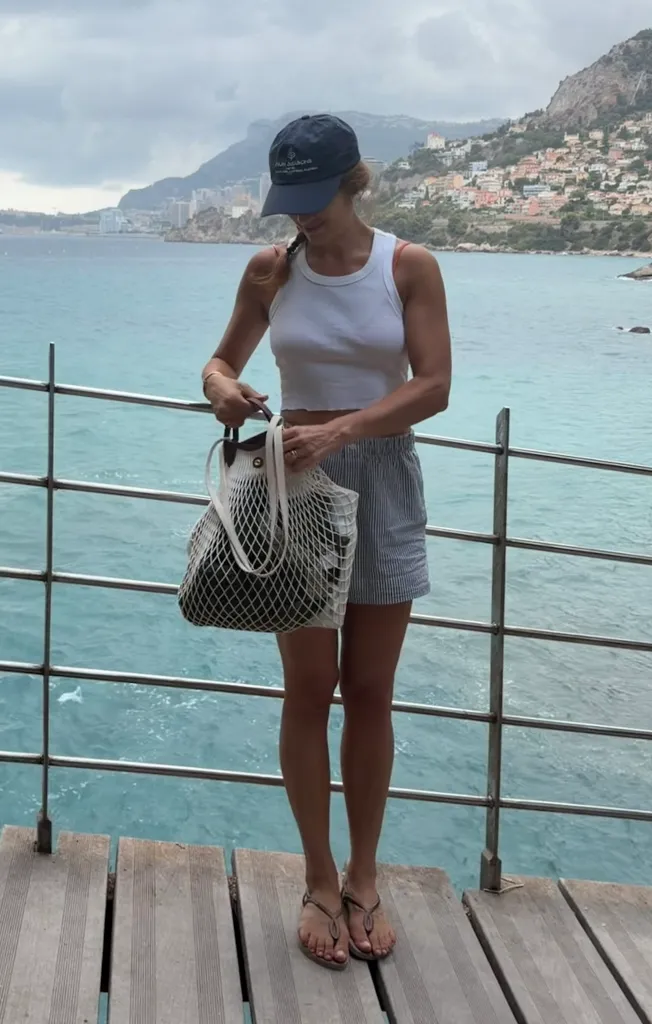 Nadia Tuma-Weldon standing by the sea in Paris, holding a netted tote bag.
