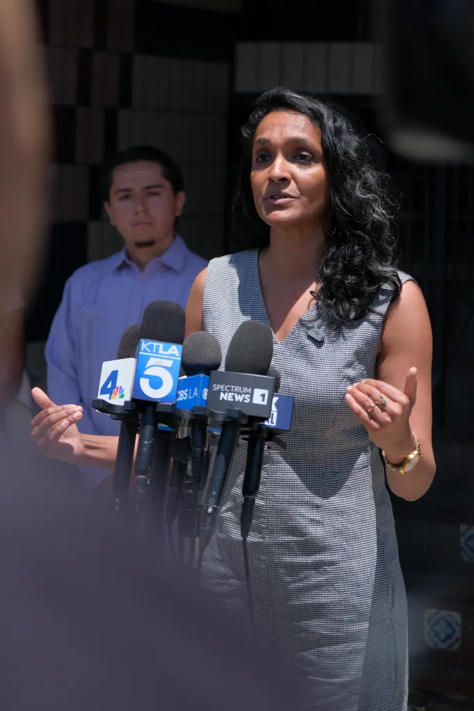 Nithya Raman speaking at El Mercadito with multiple microphones in front of her.