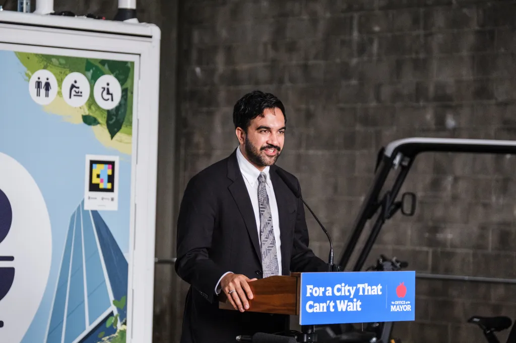 NYC Mayor Zohran Mamdani speaking at a podium with 