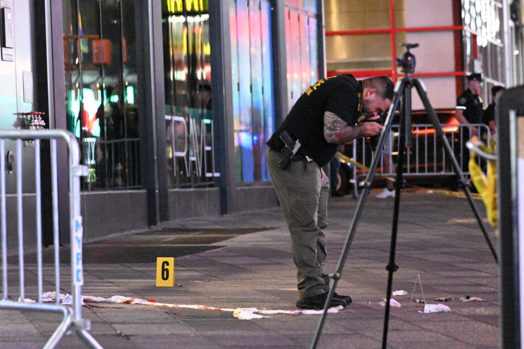 NYPD crime scene unit investigator takes photos near evidence markers on the ground in Times Square.
