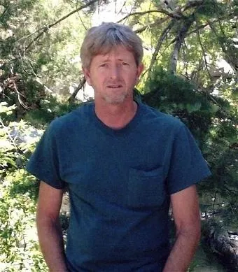 Roger Gregory Cummings, 63, standing in front of trees.