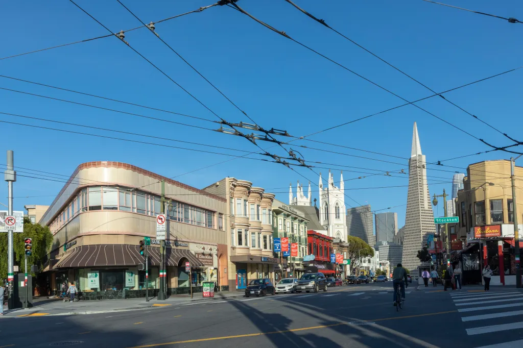 Old houses and businesses line a San Francisco street with the Transamerica Pyramid in the background.