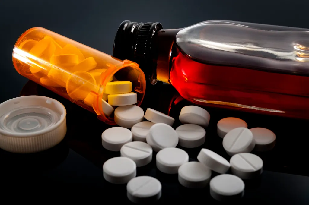 Oxycodone pills spilled from a prescription bottle next to a flask of liquor.