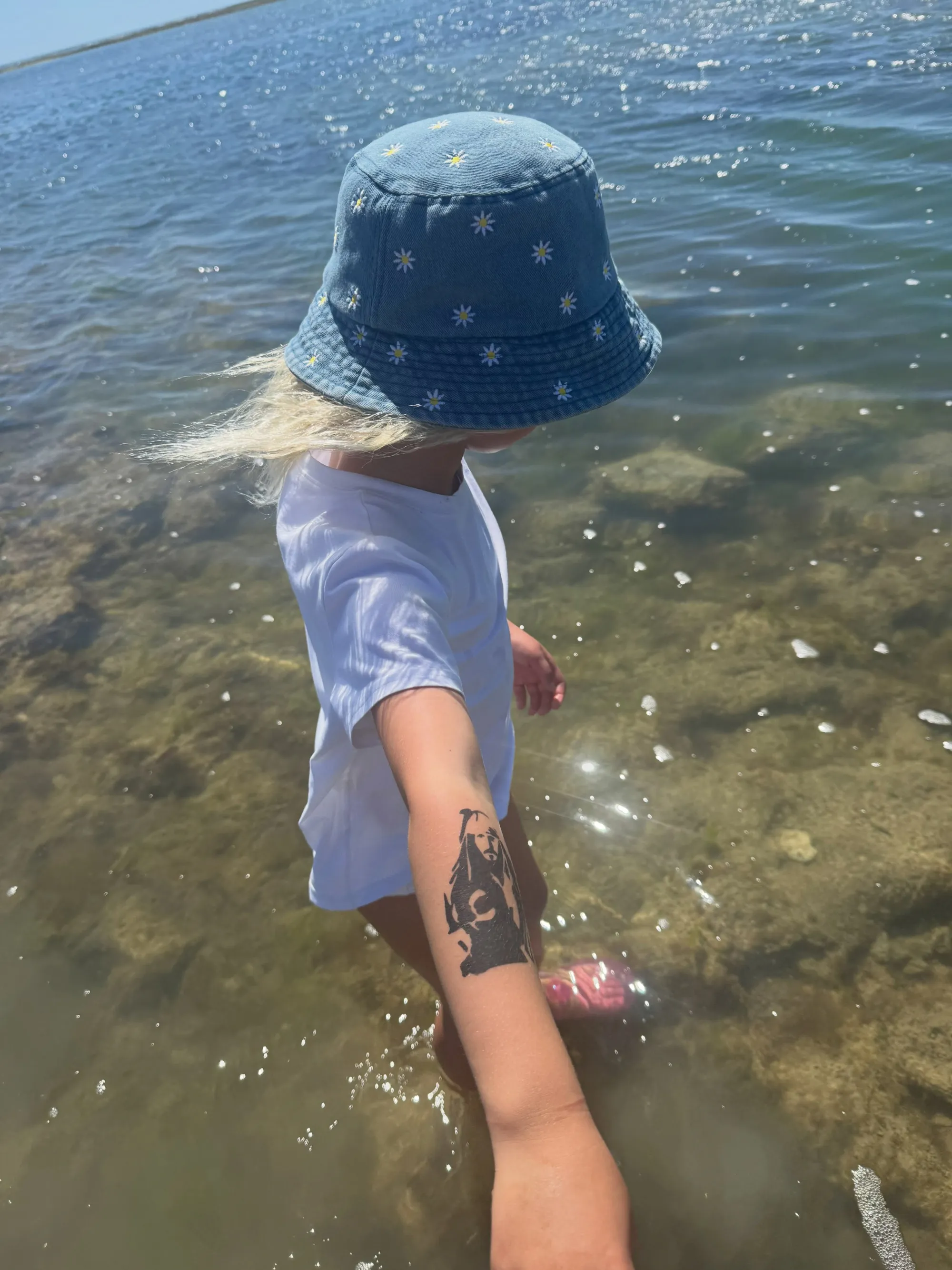 Daisy Dove showing off a Captain Jack Sparrow tattoo on her arm while standing in shallow water.