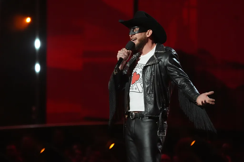 Orville Peck performing at the MTV Video Music Awards in a black cowboy hat, black mask, black leather jacket with fringe sleeves, and a white T-shirt.