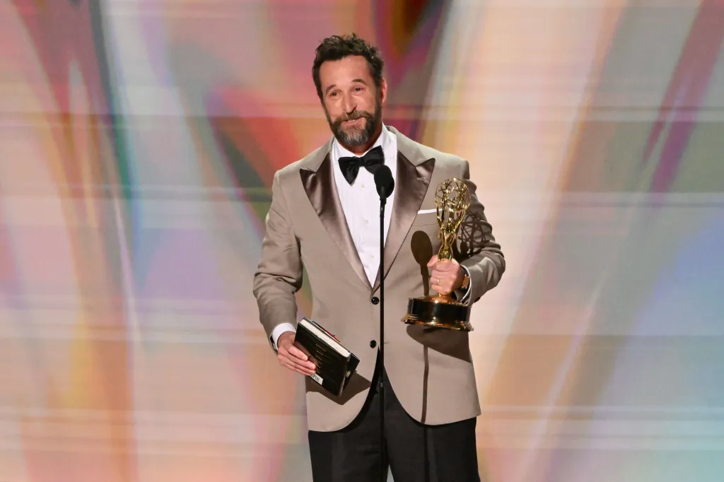 Noah Wyle holding an Emmy award and a book.