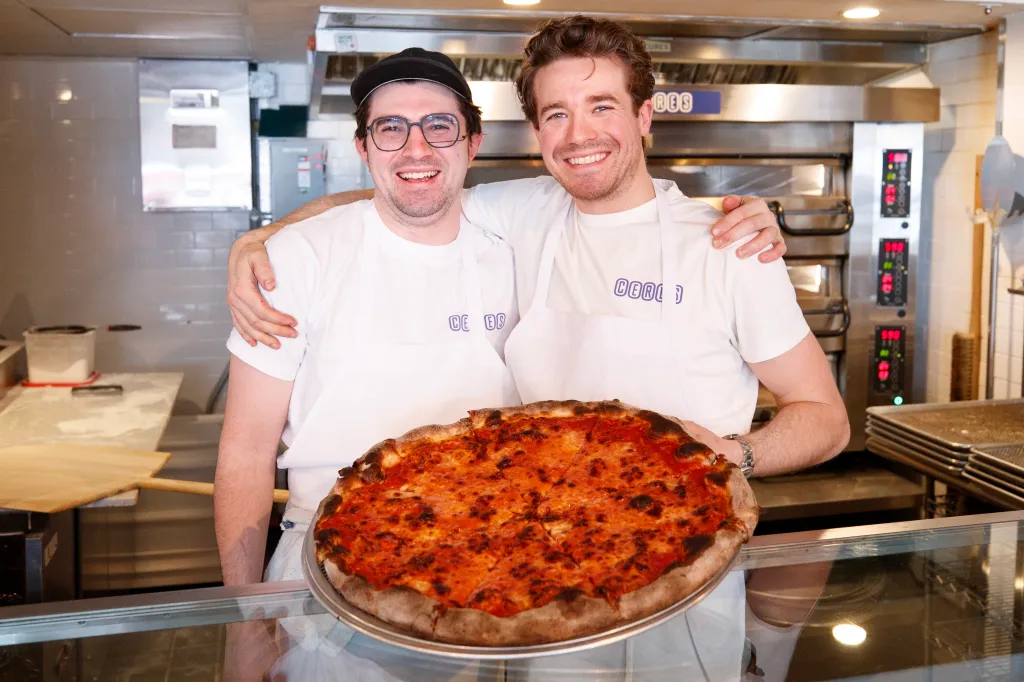 Ceres Pizza owners Jake Serebnick (left) and Julian Geldmacher (right) smile with a fresh pizza.