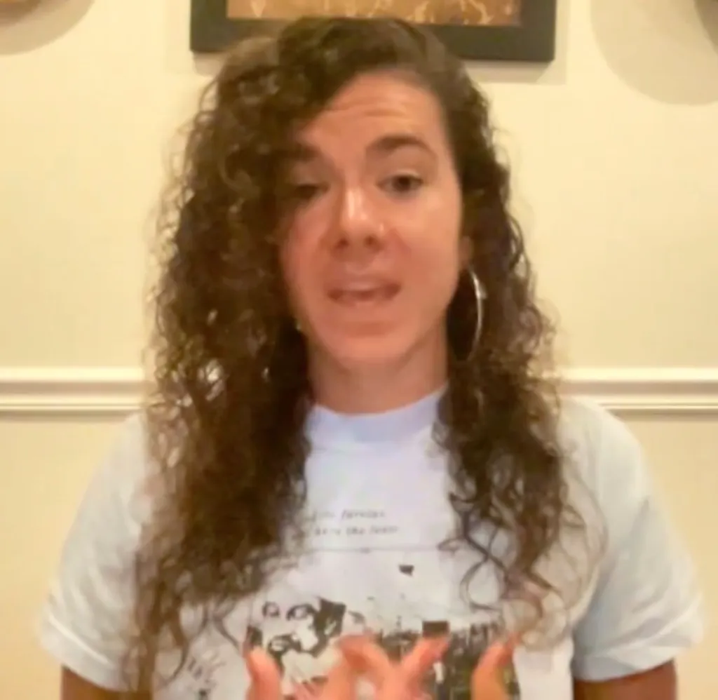 Hannah Gann, a white woman with long curly brown hair and hoop earrings, speaking.