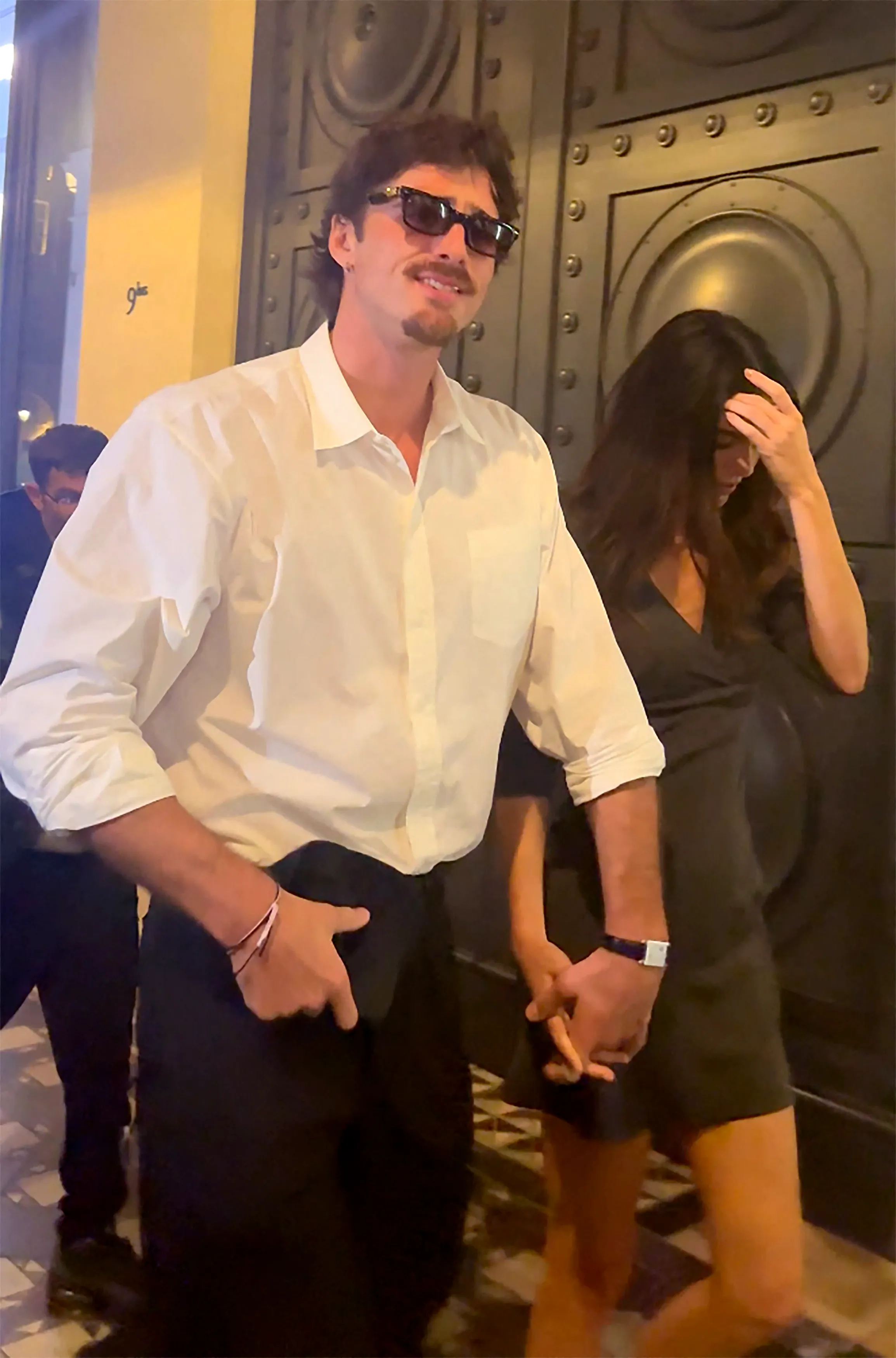 Jacob Elordi and Kendall Jenner holding hands while walking out of Hôtel Costes, with Jenner covering her face from flashing cameras.