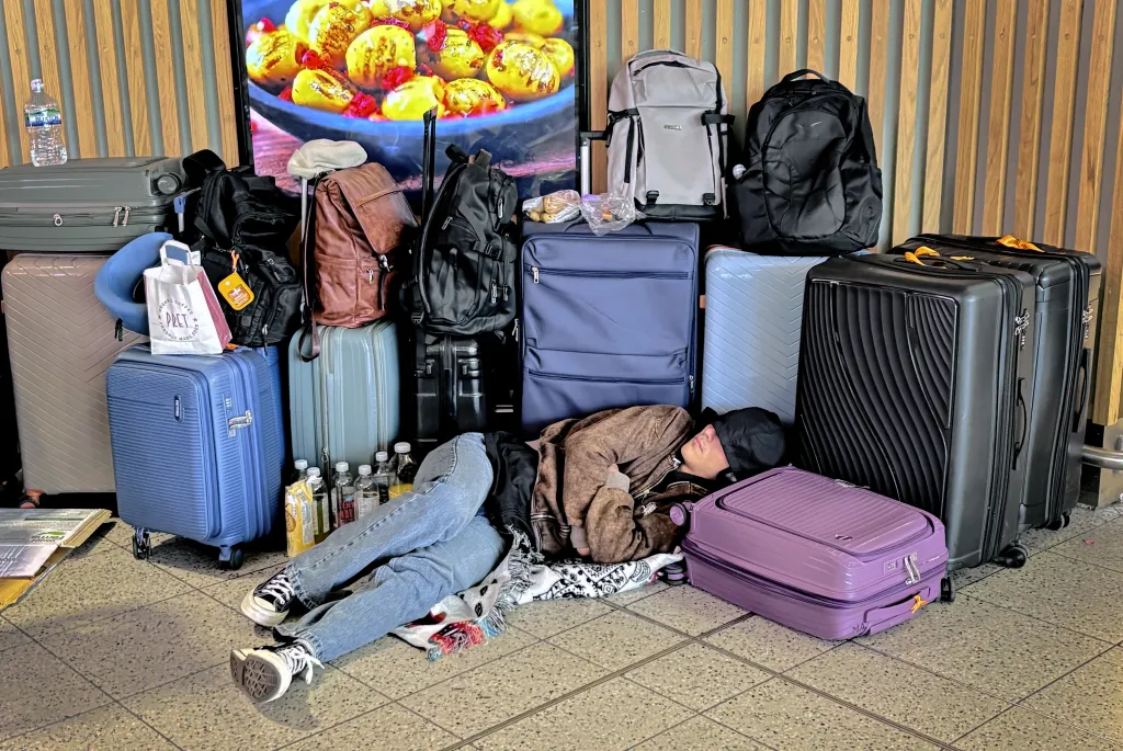 A passenger sleeps on the floor surrounded by luggage at Gatwick Airport due to a technical issue impacting air traffic control services.