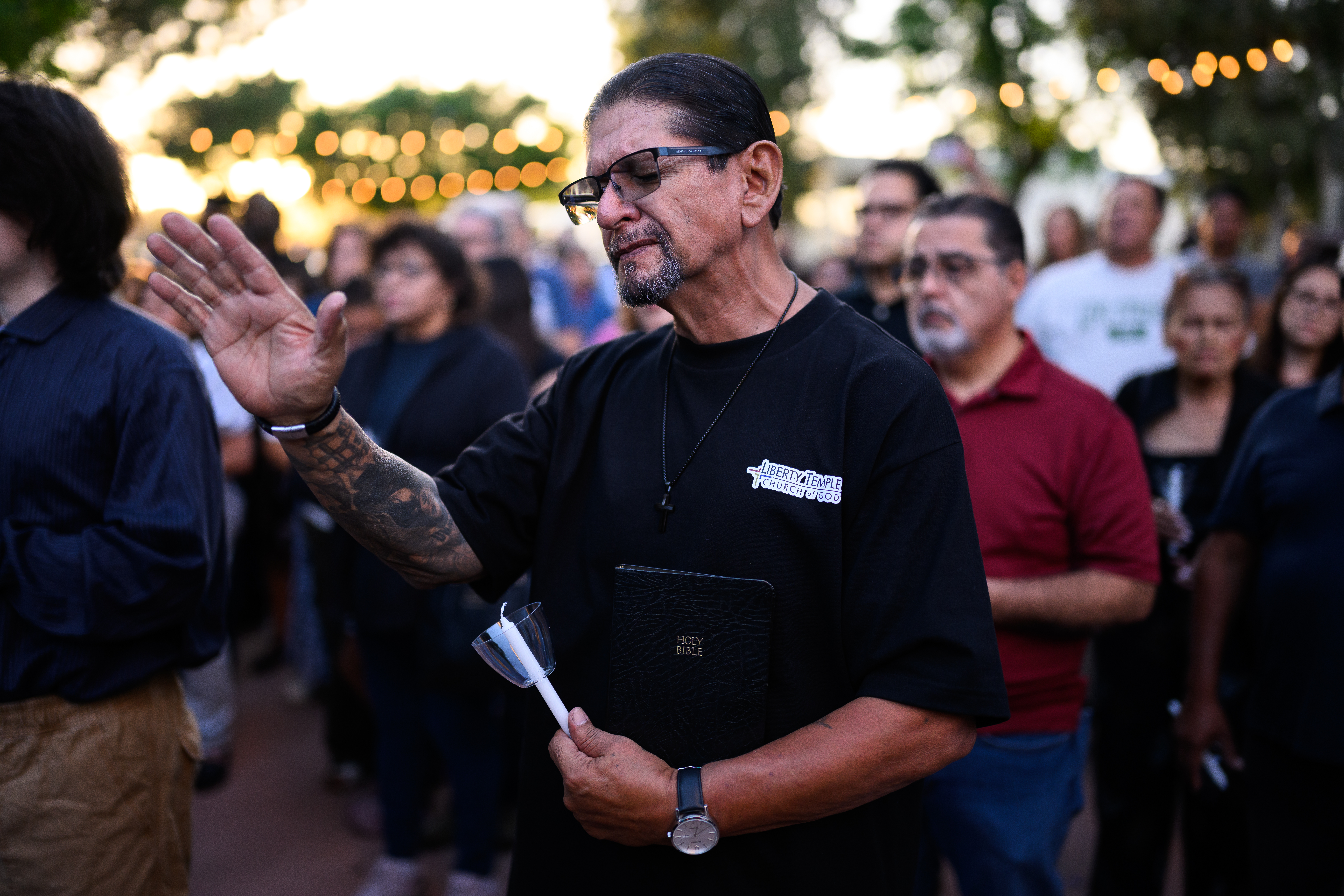 Pastor Jimmy Rocha praying during a vigil, holding a Bible and unlit candle.