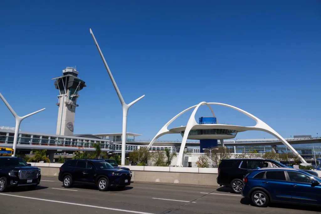 Cars drive at Los Angeles International Airport with the air traffic control tower in the background.