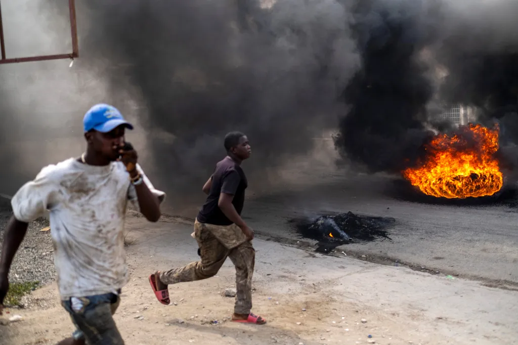 Two men run past burning tires creating thick black smoke during a protest.