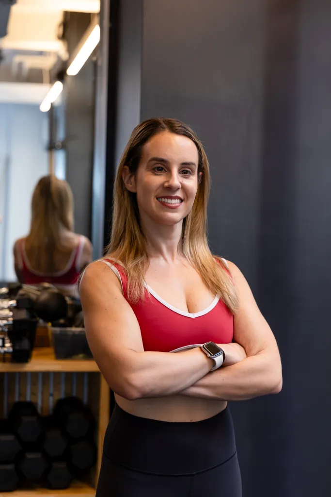 Personal trainer Sarah Cucuzzella of Aussie Fit NY poses with her arms crossed, showing muscle definition, in a gym setting.
