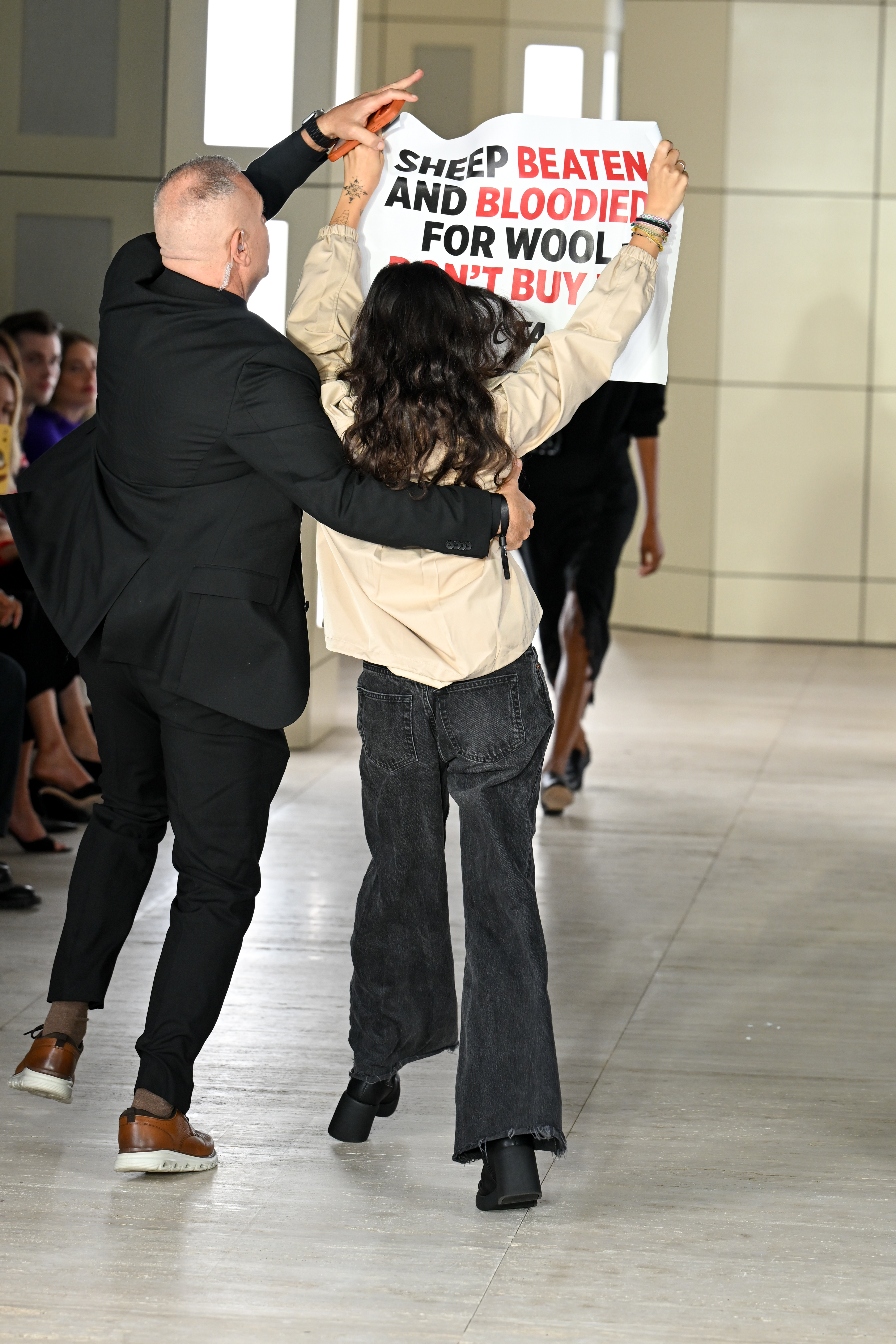 A man in a suit pulls a PETA protestor holding a sign reading