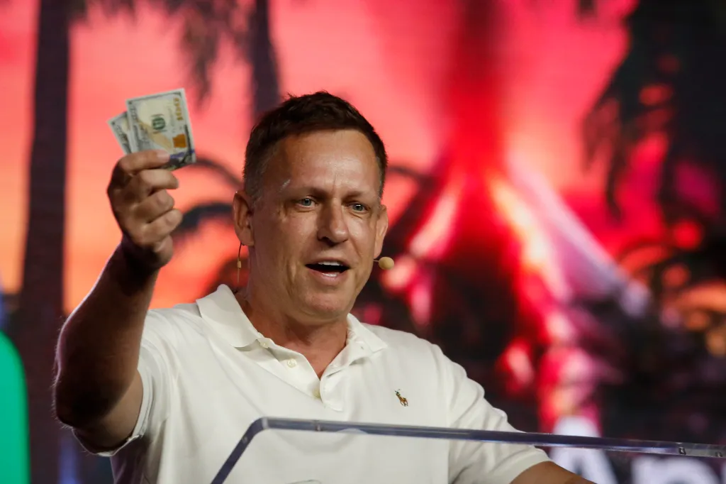 Peter Thiel holding hundred dollar bills while speaking at the Bitcoin 2022 Conference.