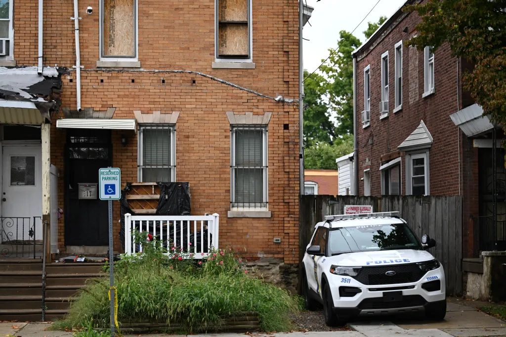 A police SUV parked in front of Eugene Horsch's brick row house in Philadelphia, with some windows boarded up.