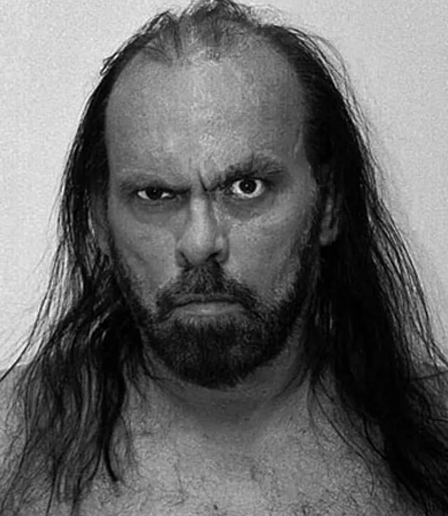 Black and white photo of RC Horsch, a man with long dark hair, a beard, and a menacing expression.