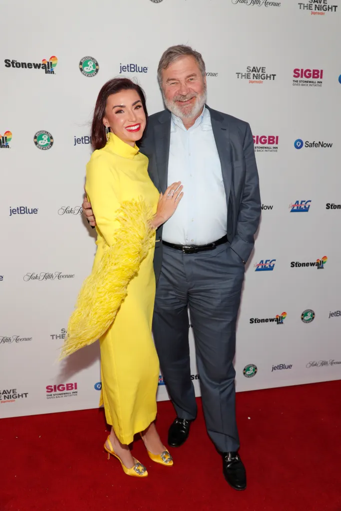Bronwyn Newport in a yellow dress and Todd Bradley in a suit pose on a red carpet at The Stonewall Inn Gives Back Initiative's Pride kickoff.