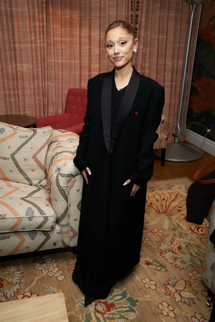 Ariana Grande attending a special screening of Wicked: For Good, wearing a long black coat over a black top and a poppy pin on the lapel.