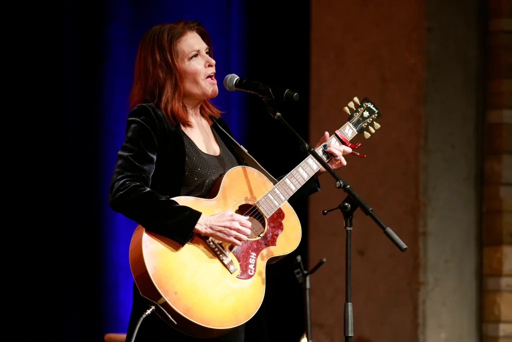 Rosanne Cash singing and playing an acoustic guitar on stage.