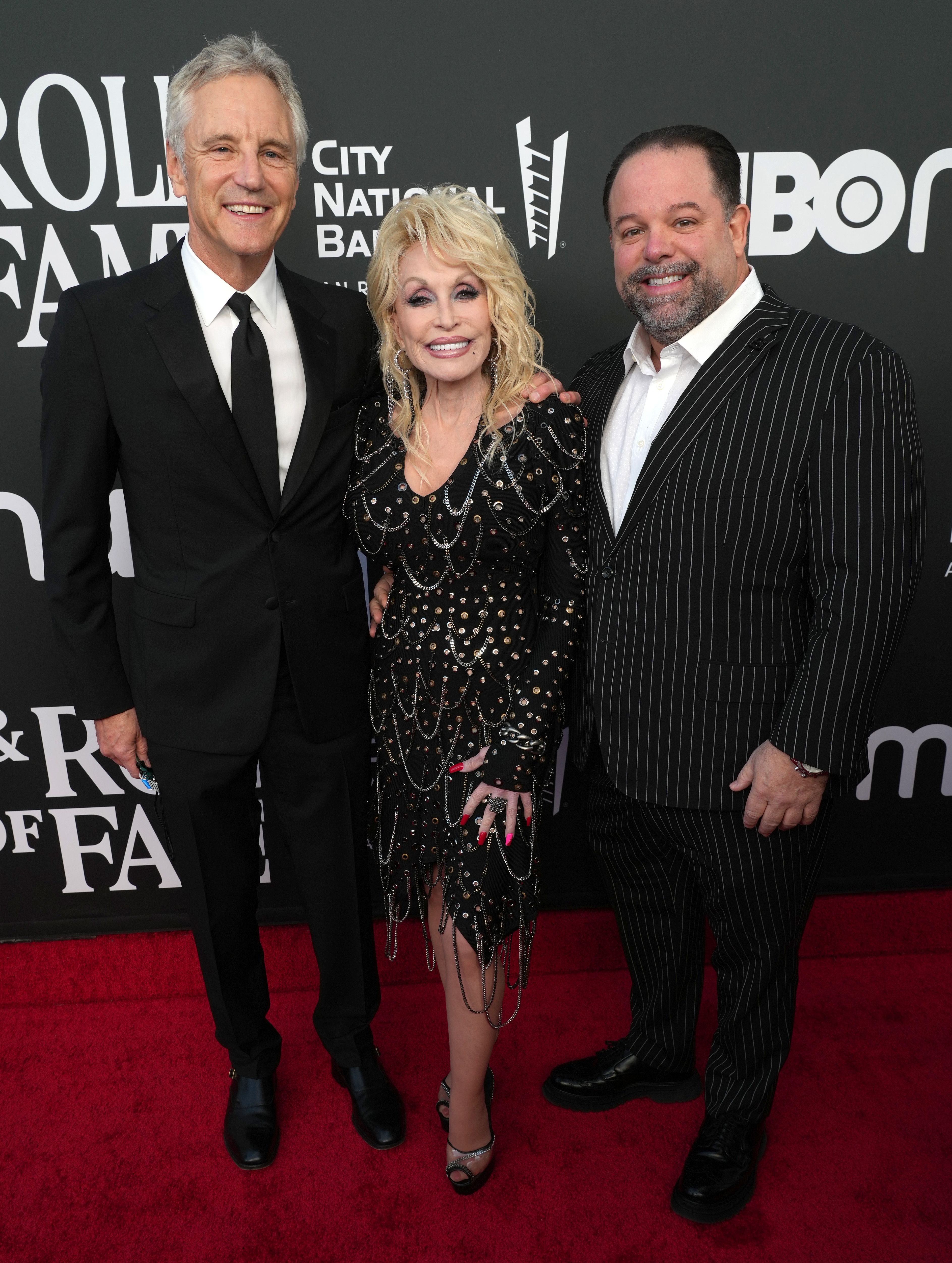 Dolly Parton, John Sykes, and Danny Nozell pose on the red carpet at the 37th Annual Rock & Roll Hall of Fame Induction Ceremony.