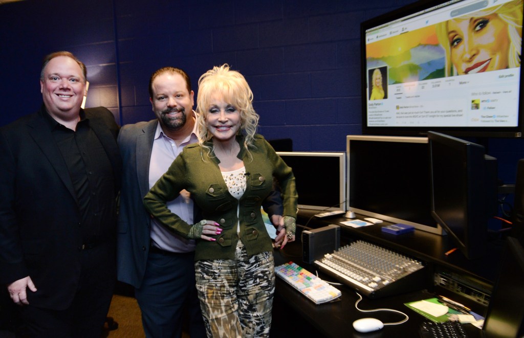Dolly Parton, her publicist Kirt Webster, and manager Danny Nozell smiling at a rehearsal space in Nashville.