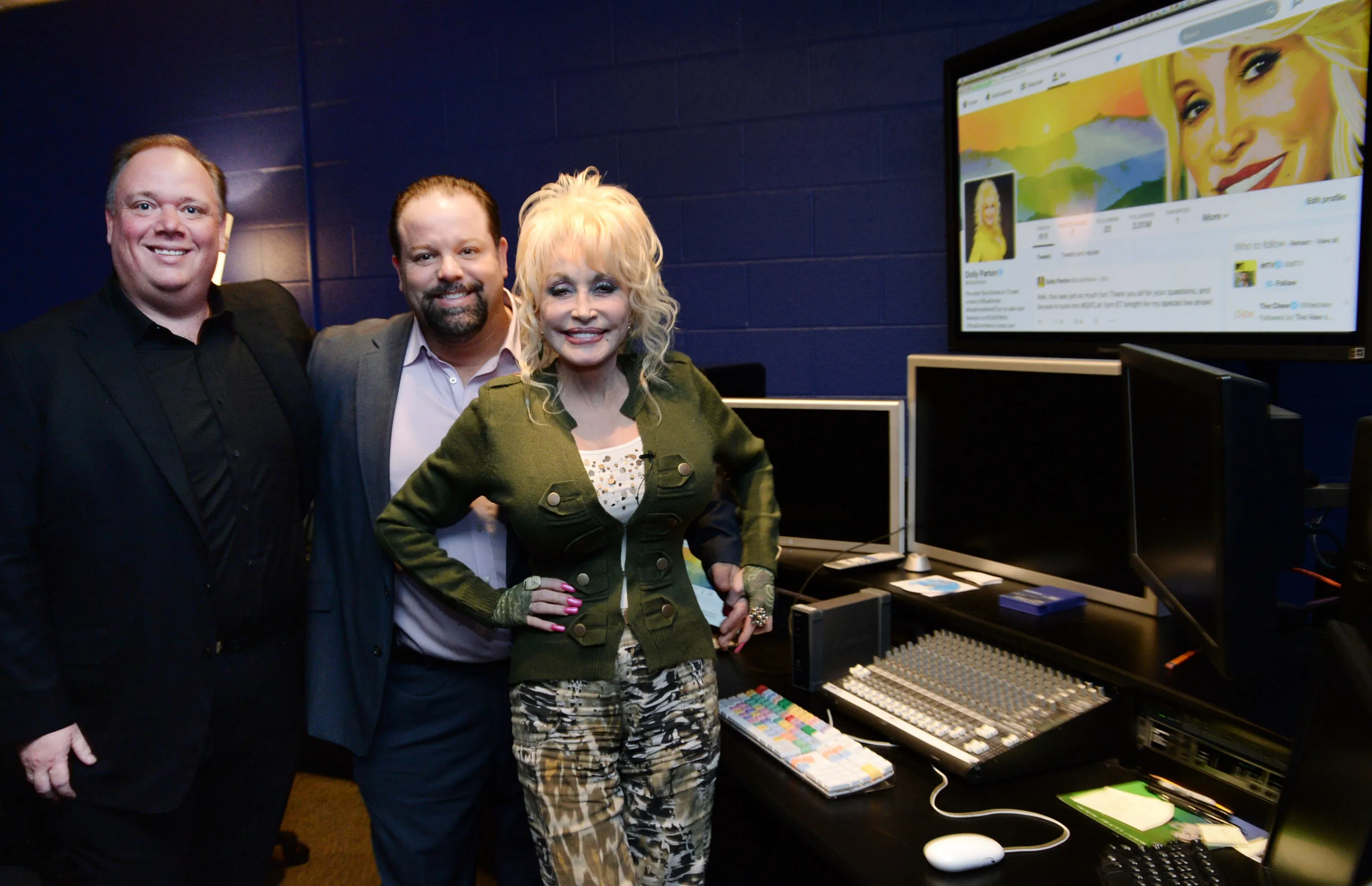 Dolly Parton with Kirt Webster and Danny Nozell in a studio, with a monitor displaying Dolly Parton's Twitter page.