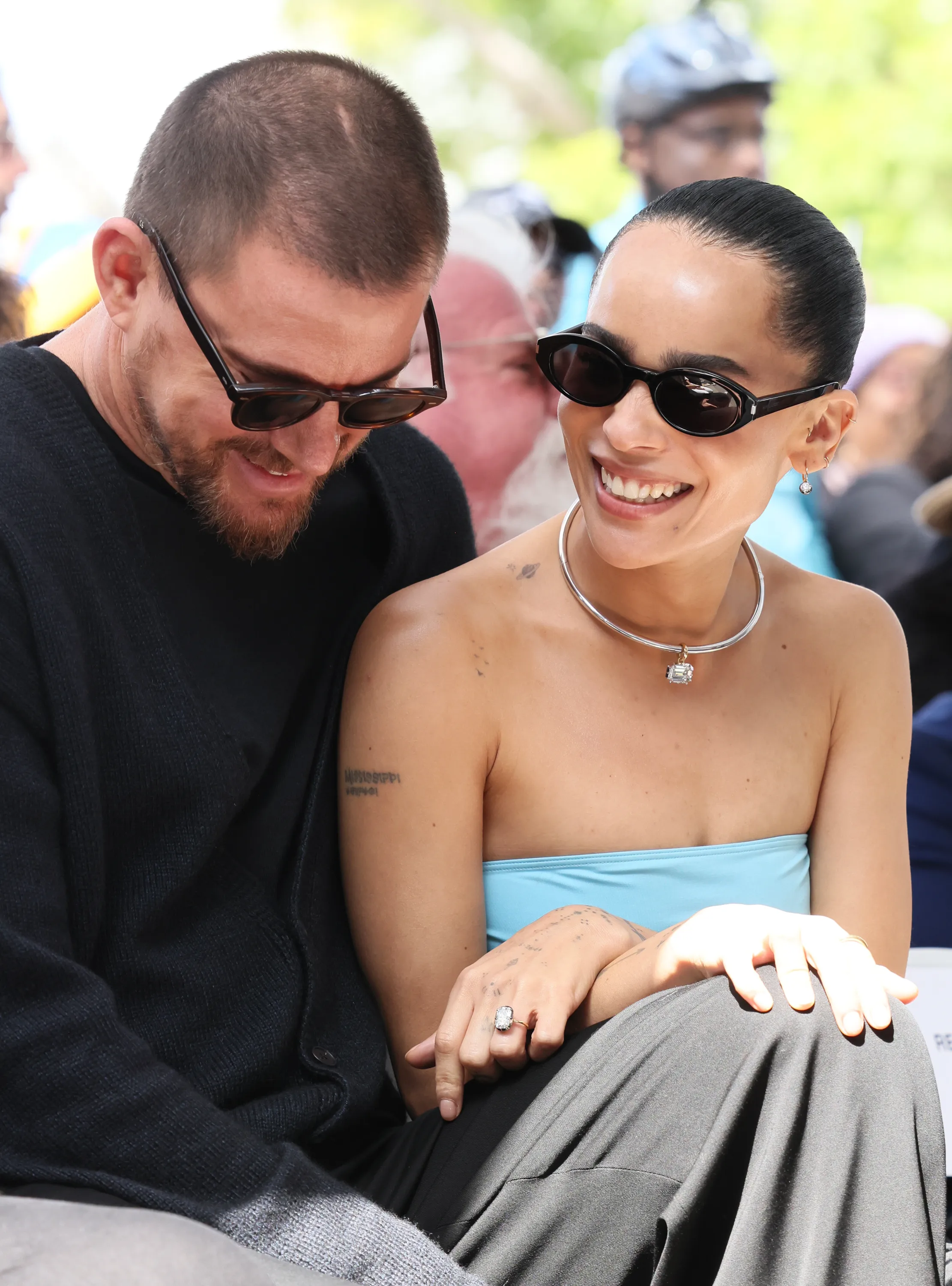 Channing Tatum and Zoë Kravitz sitting together, Tatum with a beard and sunglasses, and Kravitz smiling, wearing sunglasses, a strapless top, and a diamond necklace.