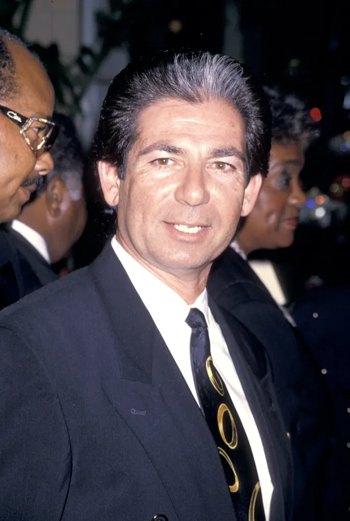 Robert Kardashian in a suit and patterned tie, smiling.