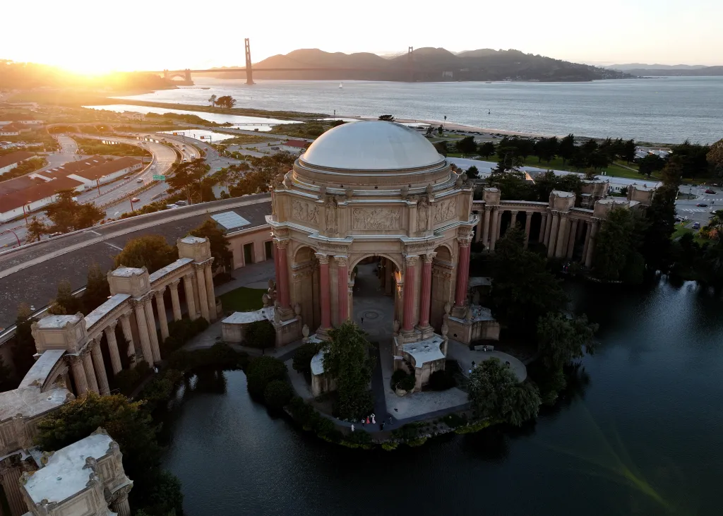 Aerial view of the Palace of Fine Arts in San Francisco at sunset, with the Golden Gate Bridge visible in the background.