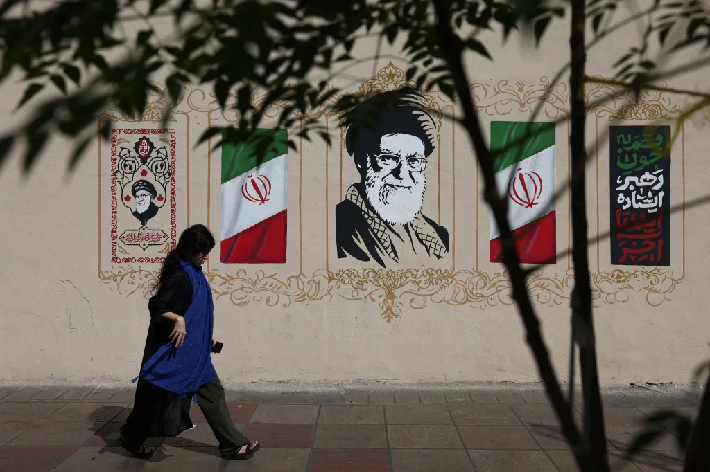 A woman walks by a mural depicting Iran's late Supreme Leader Ayatollah Ali Khamenei and Iranian flags.