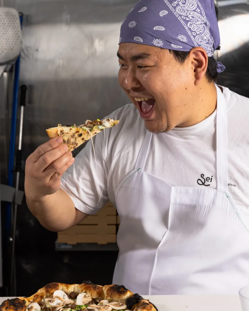 Chef at Pizzeria Sei about to take a bite of a pizza slice.