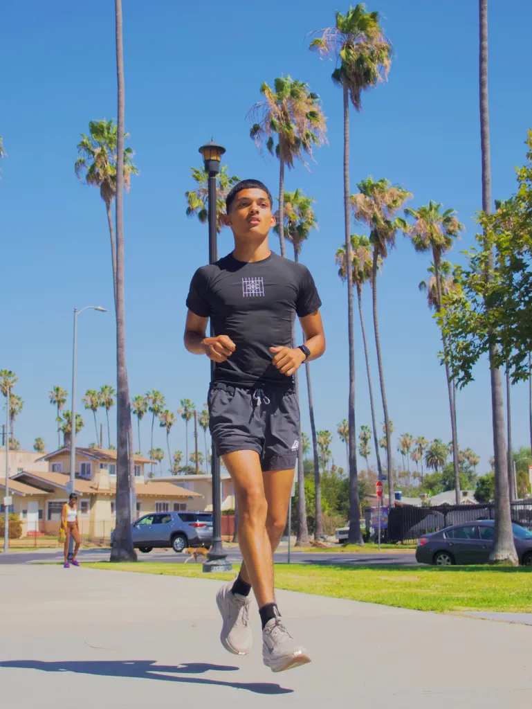 A young man in athletic wear running outdoors on a sunny day with palm trees in the background.