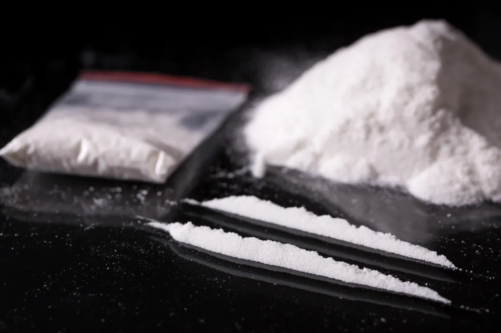 A plastic packet, two lines, and a pile of white cocaine powder on a black background.