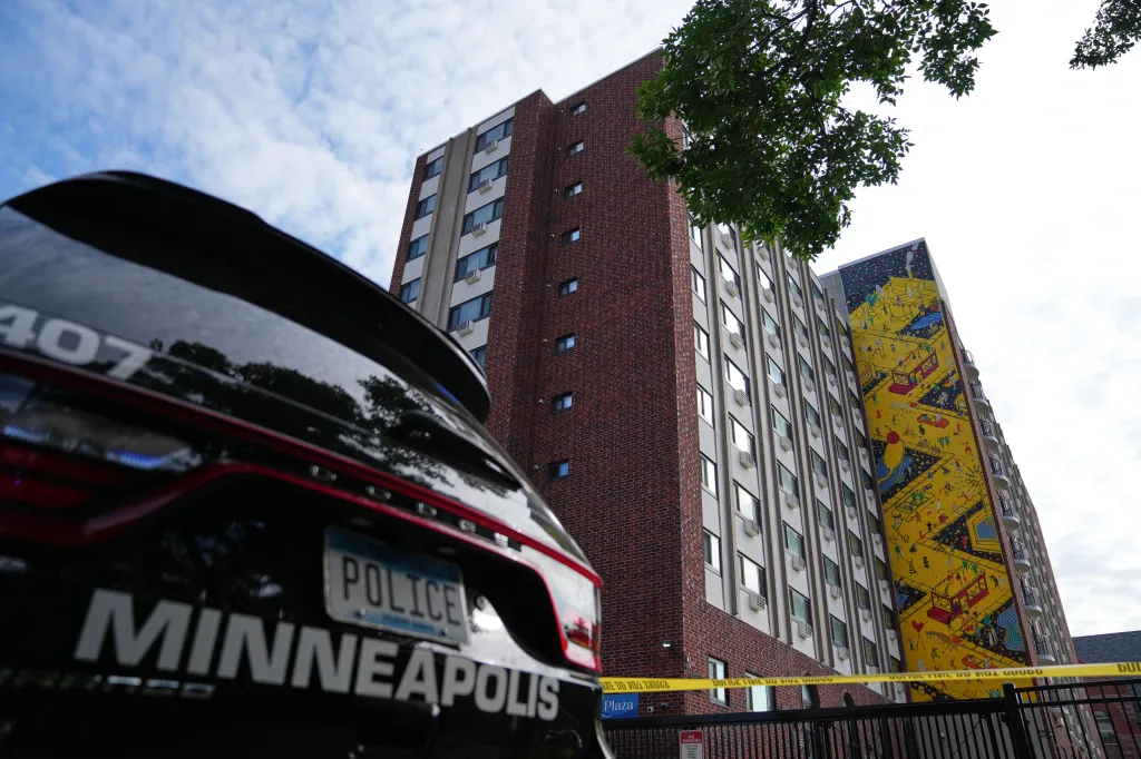 A Minneapolis police vehicle parked near an apartment building with crime scene tape.