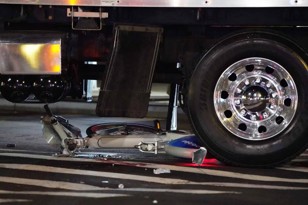 A damaged Citibike lies on the street near the wheel of a truck.