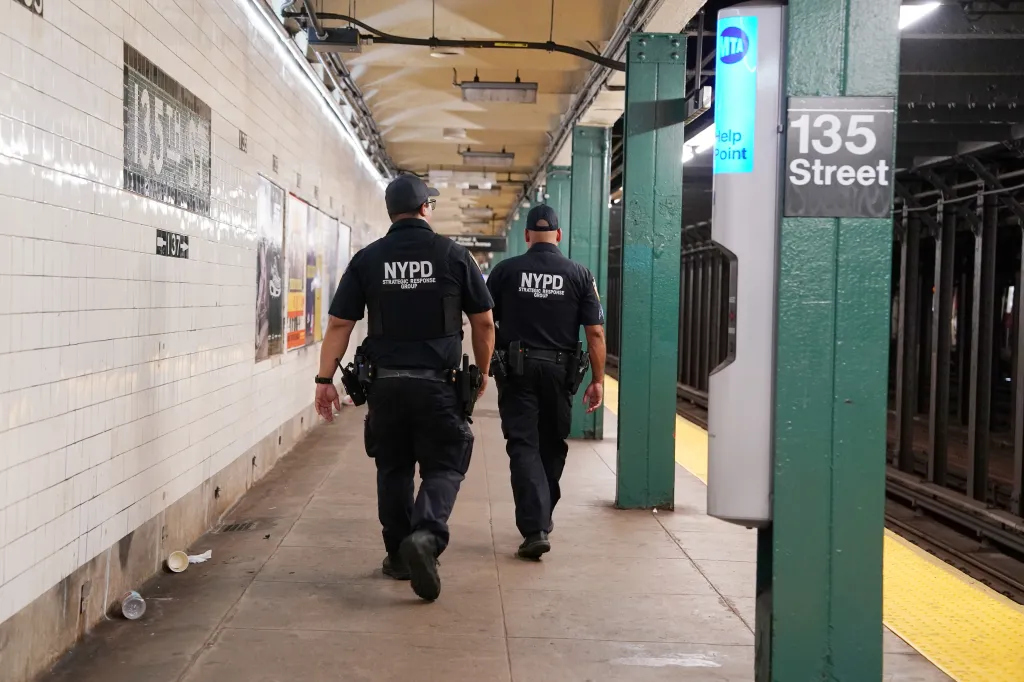 Two NYPD officers walk along a subway platform at 135th Street station.