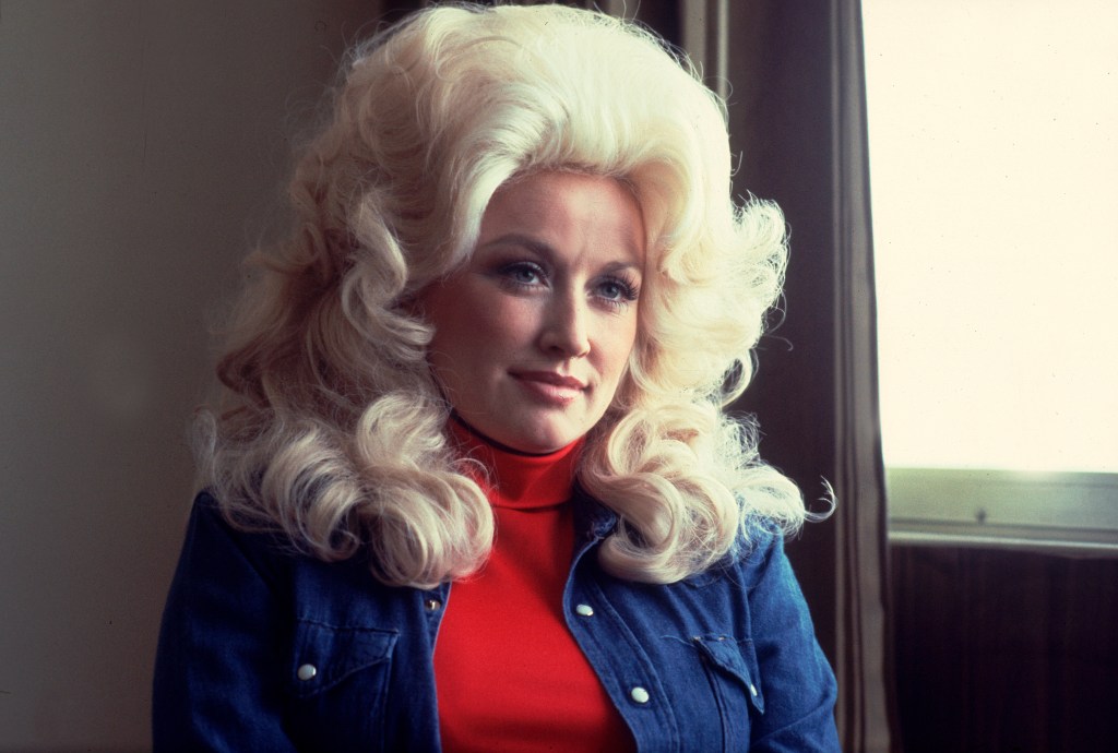 Portrait of Dolly Parton wearing a red turtleneck and denim jacket, with voluminous blonde hair.