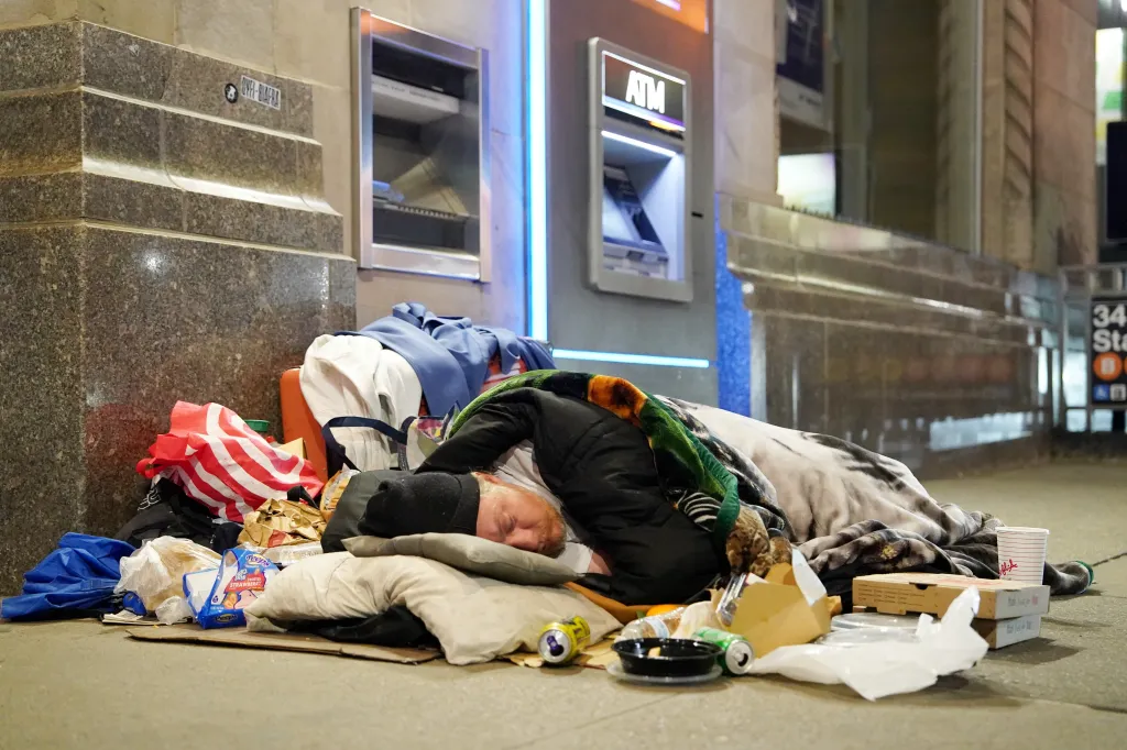 A homeless person sleeps on a New York City street, covered by a blanket.