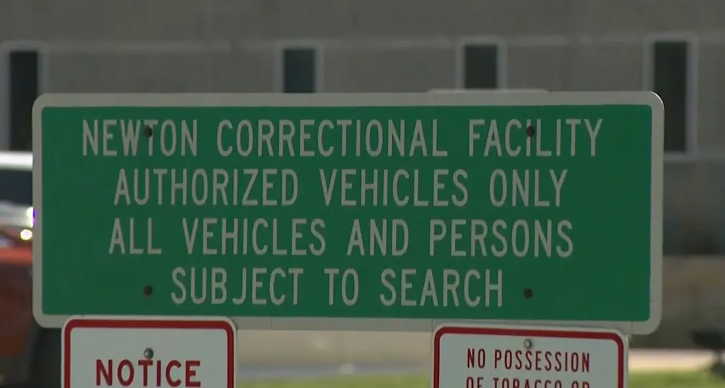 A green sign for Newton Correctional Facility stating that only authorized vehicles are allowed and all vehicles and persons are subject to search.