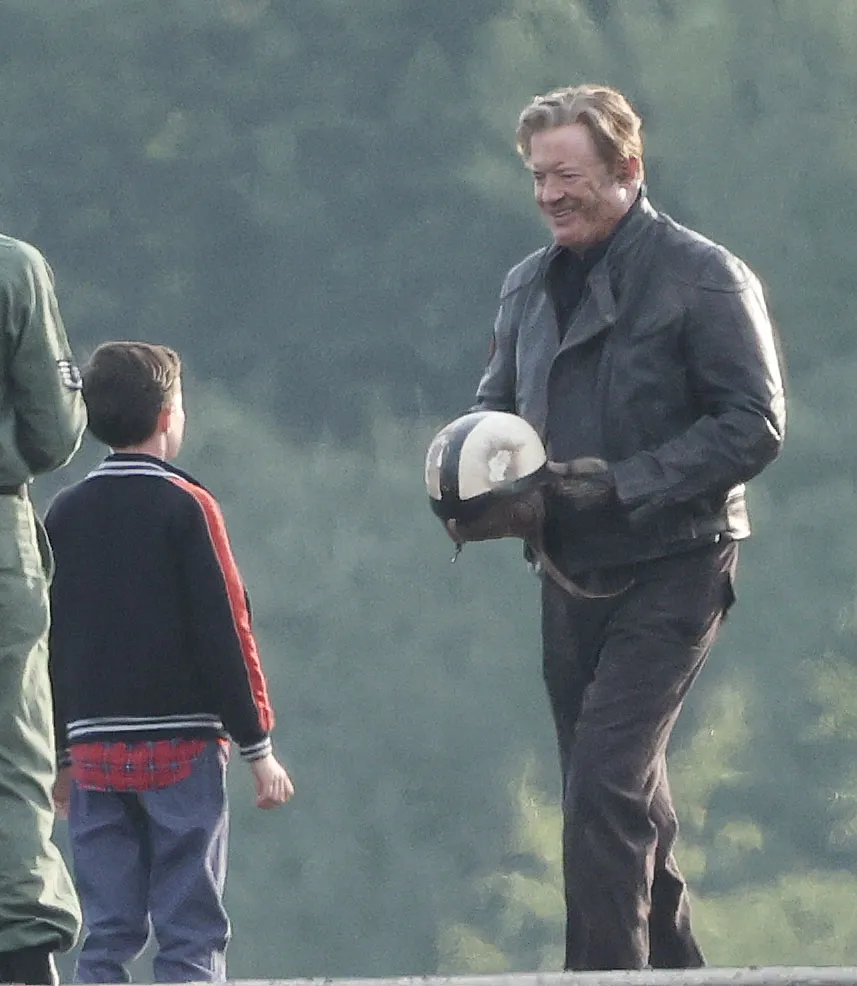 Brendan Fraser as Rick O'Connell, holding a crash helmet, speaking with a young boy on a film set.