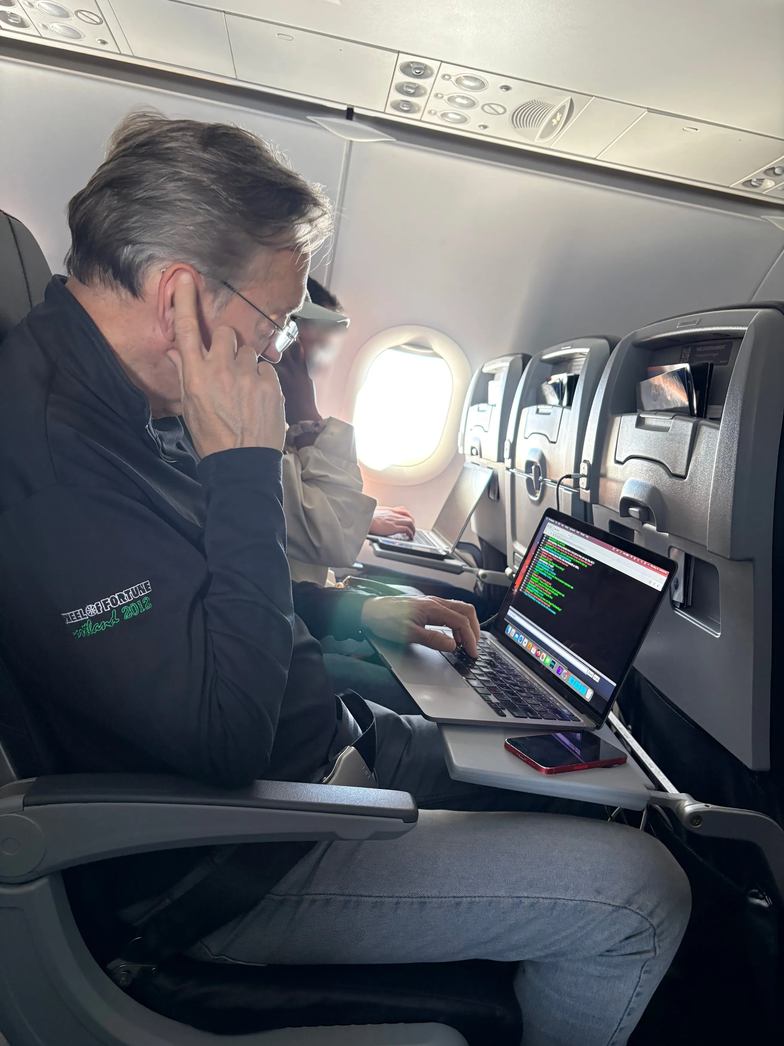 Jim Thornton on a plane, seen from his right side, wearing a black jacket with a