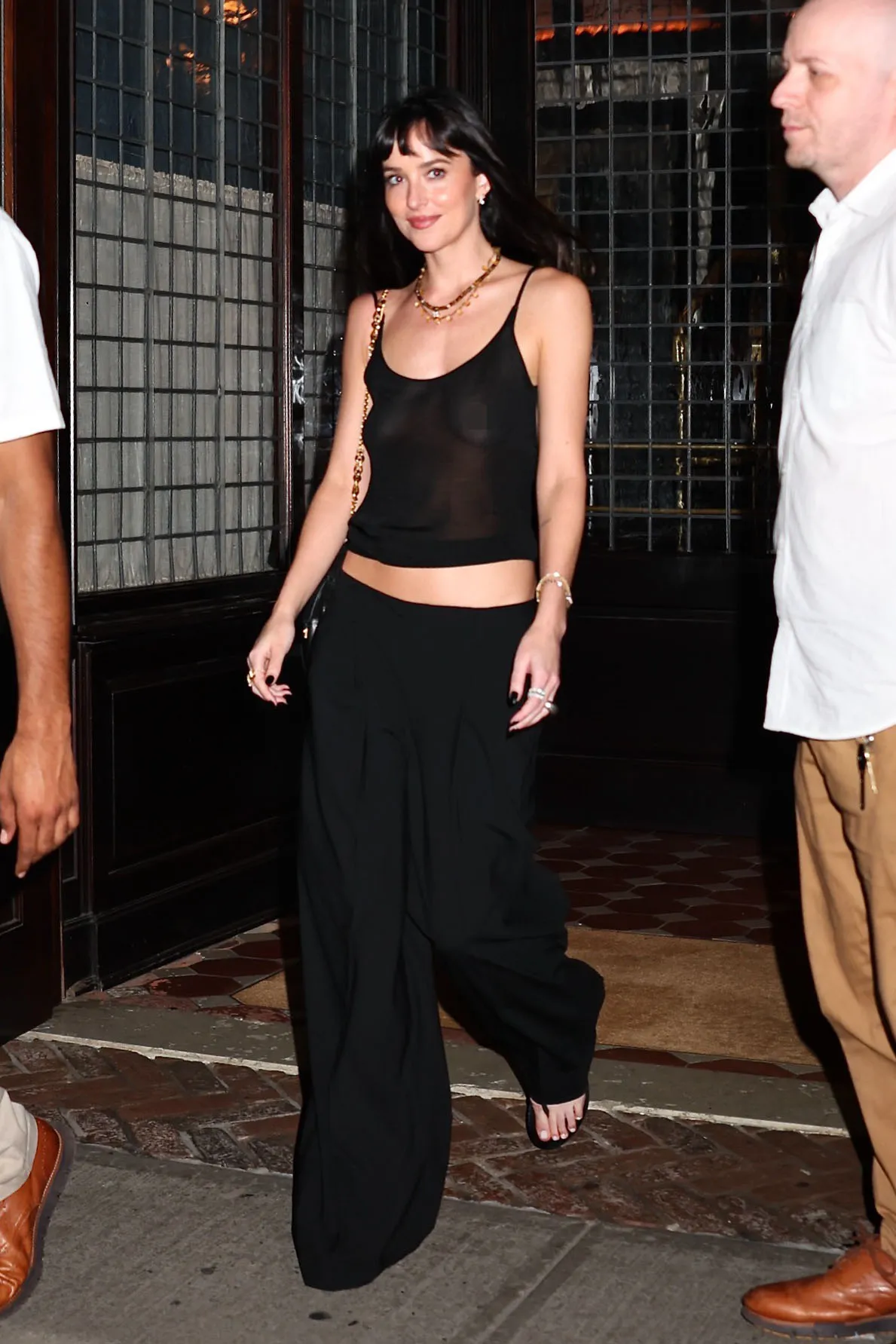 Dakota Johnson in a black transparent top and black wide-leg pants walking with friends in NYC.