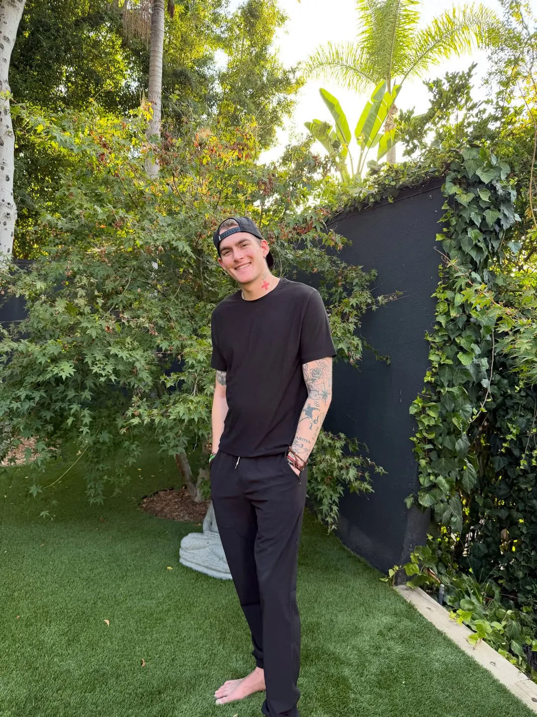 Presley Gerber, model son of Cindy Crawford and Rande Gerber, smiling outdoors in a black shirt, black sweatpants, and backward cap.
