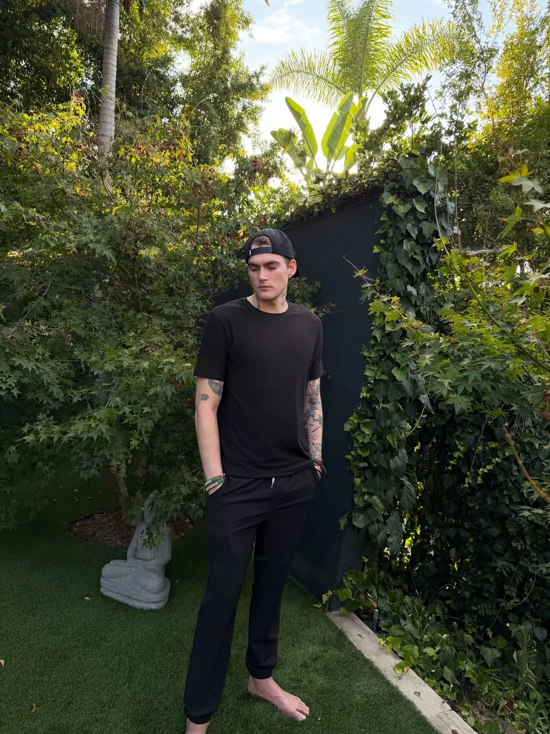 Presley Gerber standing barefoot on a lawn, surrounded by lush green foliage.